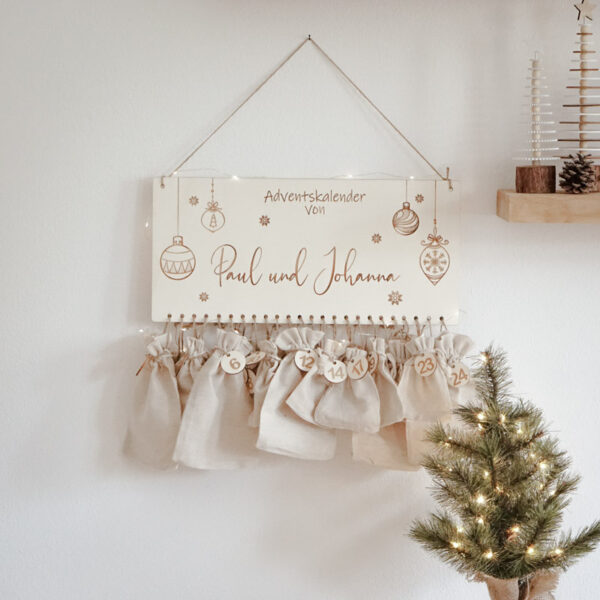 Stofftiger Adventskalender aus Holz mit 24 Stoffsäckchen, ganzer Kalender an der Wand neben einem kleinen Christbaum