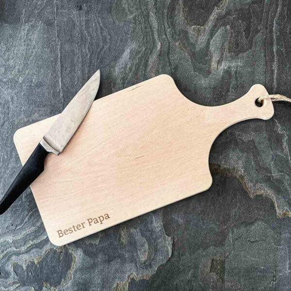 Stofftiger Schneidbrett Bester Papa aus Holz mit Gravur, daneben ein Messer auf einer Schieferplatte