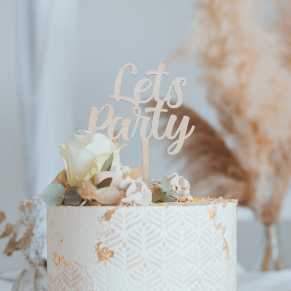 Stofftiger Caketopper Lets Party aus Holz auf einer weißen Torte mit Rosen und Pampasgras