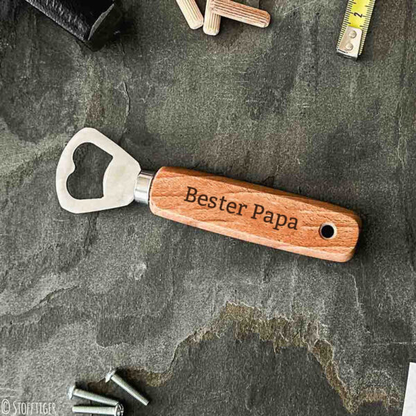 Stofftiger Flaschenöffner Bester Papa mit graviertem Holzgriff, liegt auf einer Schieferplatte