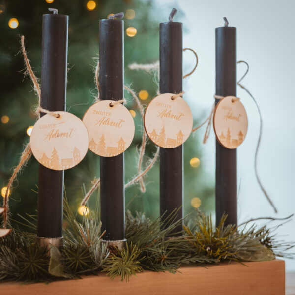 Stofftiger Zahlenanhänger Advent Häuser aus Holz, vier Anhänger an schwarzen Stabkerzen vor dem Christbaum