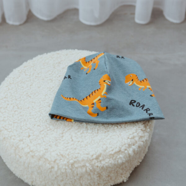 Stofftiger Haube Dinos, hellblaue Jerseyhaube mit Dinomuster auf einem Kissen