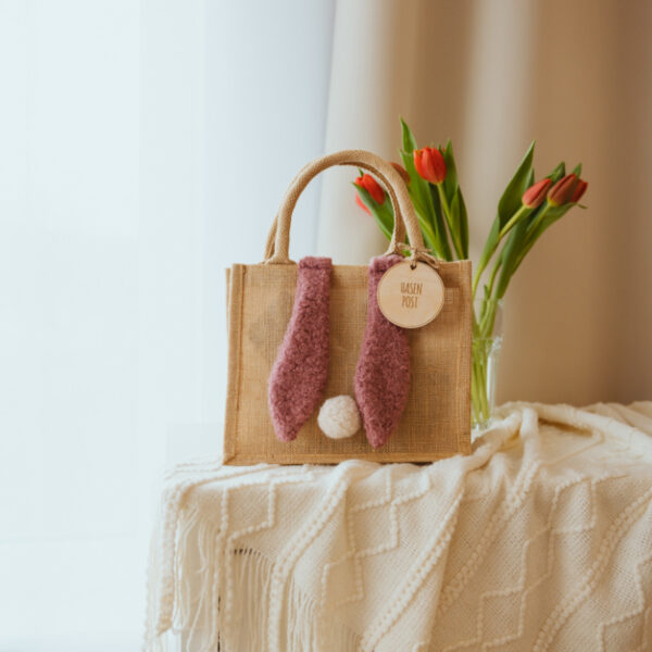 Stofftiger Osterkörbchen Jute mit Hasenohren in Altrosa und Holzanhänger, daneben Tulpen