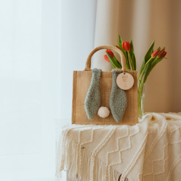 Stofftiger Osterkörbchen Jute mit Hasenohren in Mint und Holzanhänger, daneben rote Tulpen