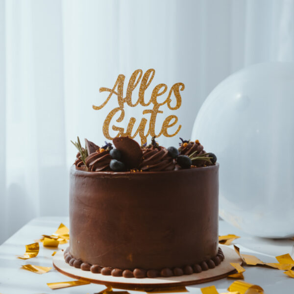 Stofftiger Caketopper in verschiedenen Farben, Schriftzug Alles Gute in Gold auf einer Schokotorte