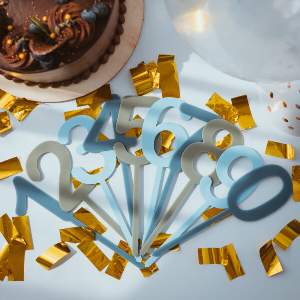 Stofftiger Caketopper Zahlenset mehrfärbig Blau, alle Zahlen in Blau- und Grautönen aufgefächert auf goldenem Konfetti