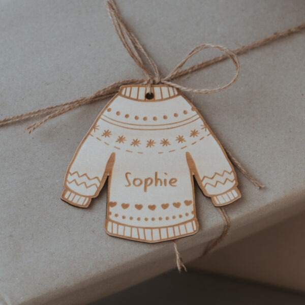 Stofftiger Weihnachtsanhänger Pullover aus Holz mit Name Sophie, Nahaufnahme mit Juteschnur auf Geschenkpapier