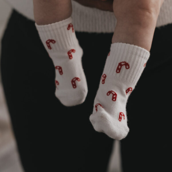 Eulenschnitt Babysocken Zuckerstangen, an Babybeinen getragen, weiß mit roten Zuckerstangen
